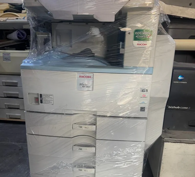 A refurbished Ricoh Aficio copier wrapped in plastic, next to other machines in the store